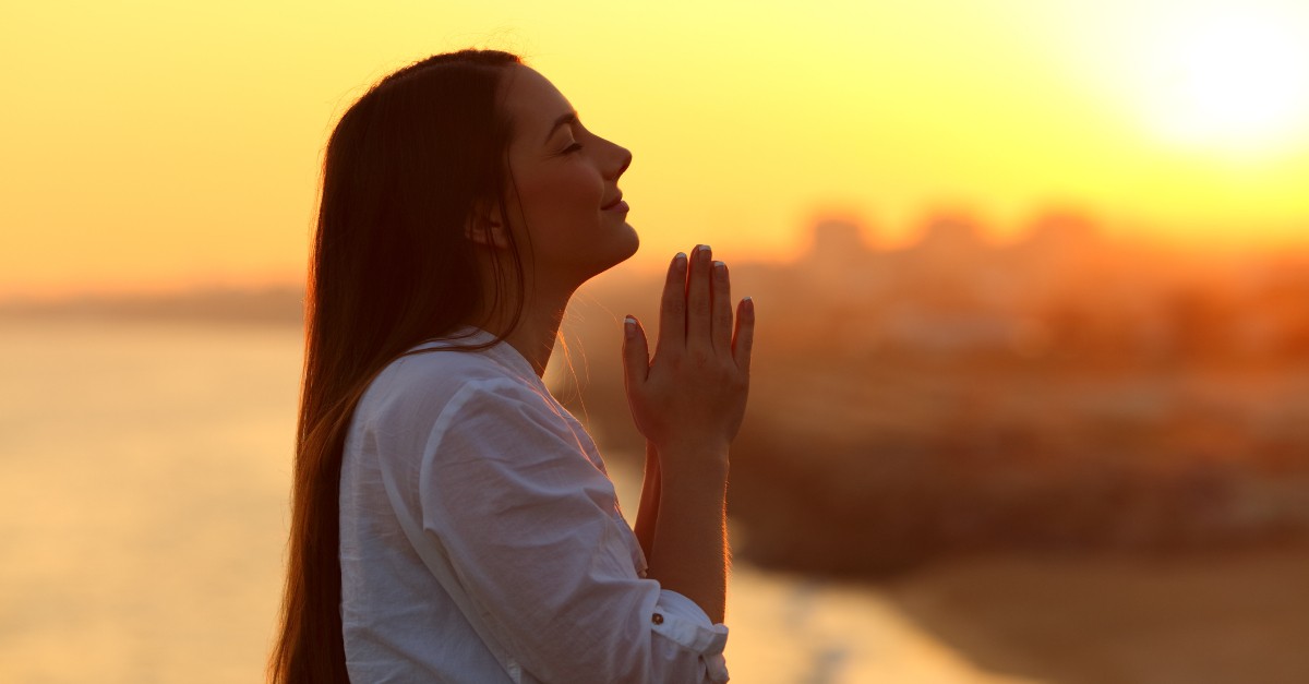 Woman praying outside under sunset